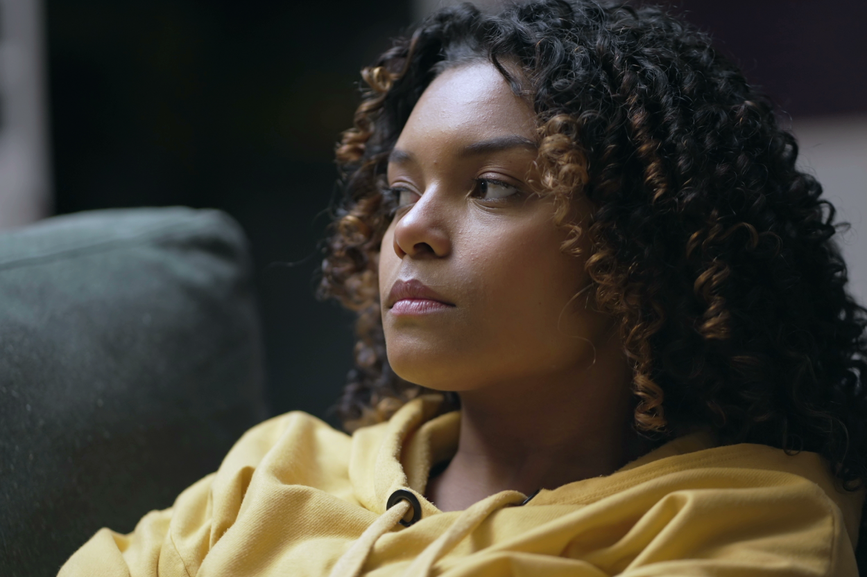 Black woman in a yellow shirt staring off to the side.